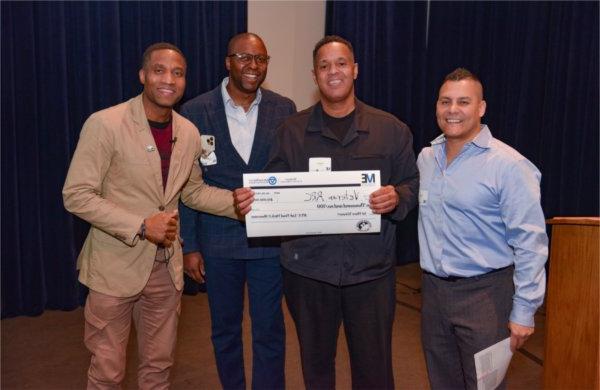 four people in row, two in center holding oversized check